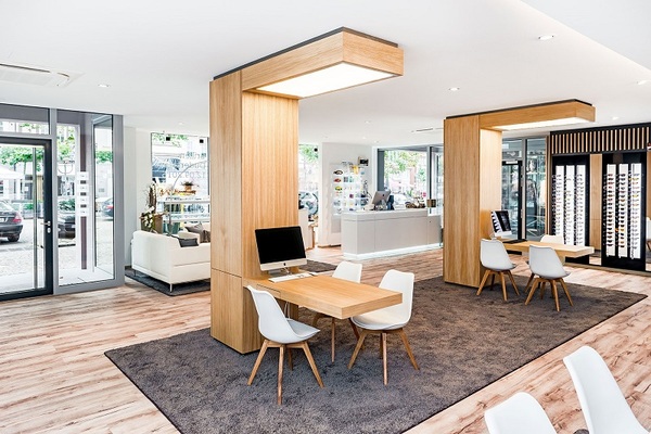 Modernes, helles Optikergeschäft mit Holzmöbeln, Beratungstischen und Brillenauswahl.